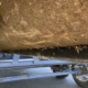 Underside of a muddy boat hull on a blue trailer, with small barnacles along the bottom edge.