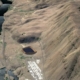 Aerial view of a river canyon with a dam on the left and three brown oval reservoirs on a hillside to the right, connected by winding roads.